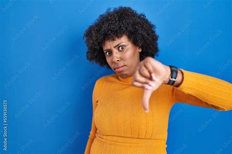 Black Woman With Curly Hair Standing Over Blue Background Looking Unhappy And Angry Showing