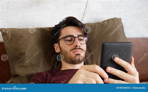 Hombre Joven Que Miente En Cama Y Que Lee El Ebook Foto De Archivo