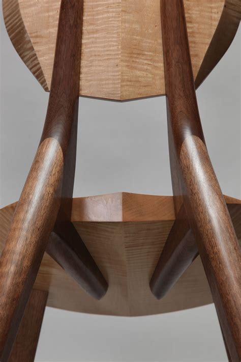 The Back Side Of A Wooden Chair With Two Bent Legs And Wood Grained Seat