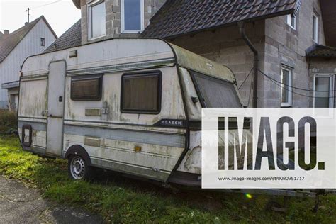 An Old Rotten Caravan Is Standing In Front Of A New Building Near Sankt