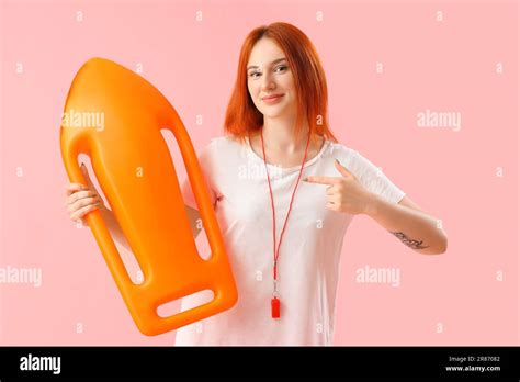 Female Lifeguard Pointing At Rescue Buoy On Pink Background Stock Photo