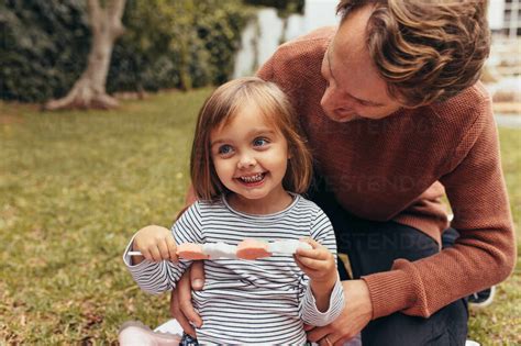 Lächelndes Mädchen sitzt mit ihrem Vater im Freien und hält eine