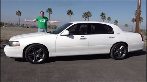 a man standing next to a white car in a parking lot with palm trees behind him