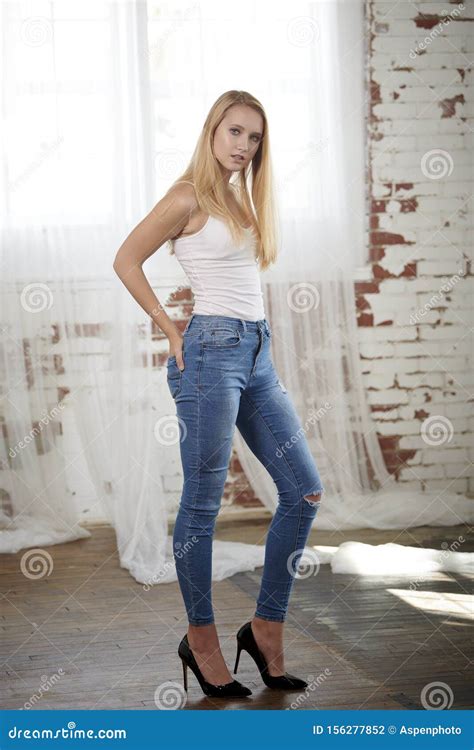 Mooie Blonde Tieners Stelt Zich Voor In Studio Met Een Witte Tank En Spijkerbroek Stock Foto