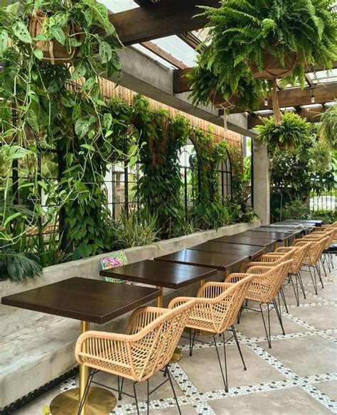 An Outdoor Dining Area With Wicker Chairs And Wooden Tables Surrounded