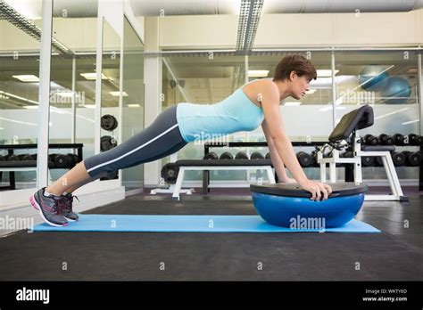 Fit Brunette Using Bosu Ball In Plank Position At The Gym Stock Photo
