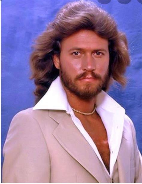 A Man With Long Hair And Beard Wearing A Tan Suit Jacket In Front Of A