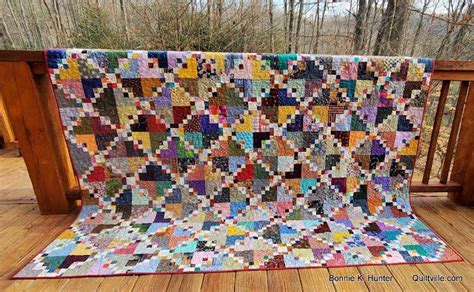 A Multicolored Quilt Sitting On Top Of A Wooden Deck In Front Of Trees