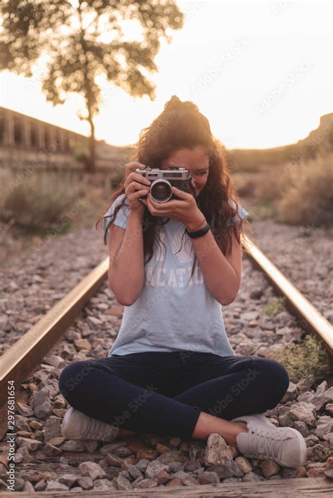 Chica joven con cabello largo sentada en las vías del tren con cámara