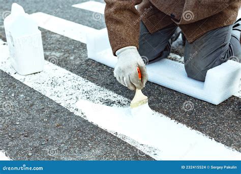 A Man Paints With A Brush On The Asphalt Markings For A Pedestrian