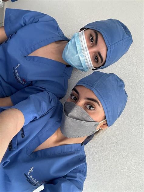 Two Doctors In Scrubs And Masks Standing Next To Each Other Looking At