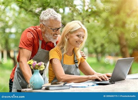 Happy Mature Spouses Using Laptop Computer While Sitting At Garden