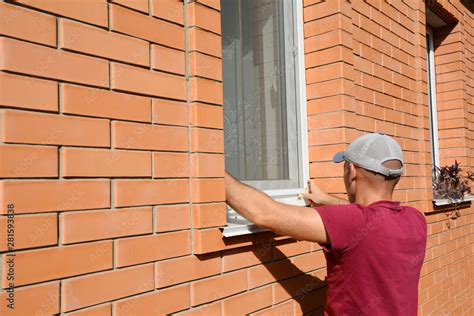 Man installing mosquito net, mosquito wire screen on brick house window ...