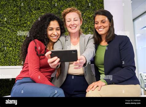 Three Young Women As Friends With Smartphones Take A Selfie For Social