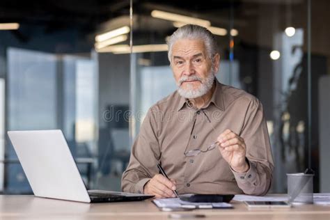 A Mature Businessman Works In An Office Focusing On Tasks With A Laptop And Paperwork At His