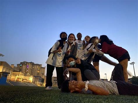 A Group Of People Standing And Laying On The Grass In Front Of A