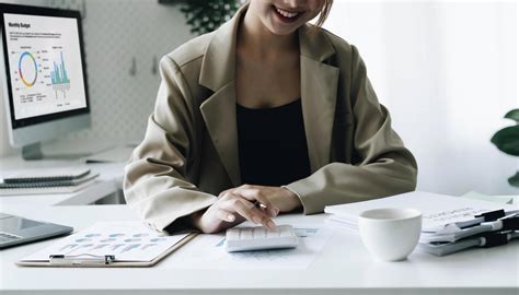 Smiling female accountant using calculator while sitting at office desk with digital tablet and ...