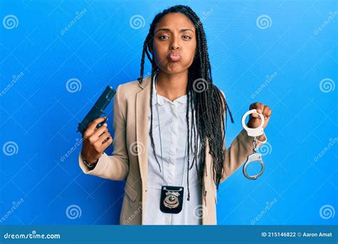 African American Police Woman Holding Gun And Handcuffs Puffing Cheeks