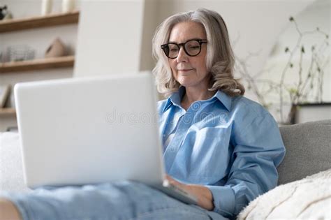 Smiling 50s Mature Woman Sitting On Sofa Using Laptop Working