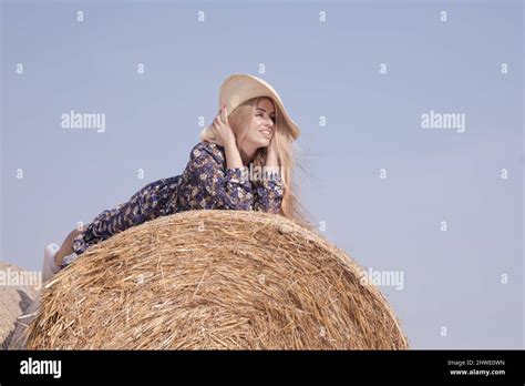 Une jeune fille blonde aux cheveux longs dans un chapeau blanc se repose et pose près des gerbes