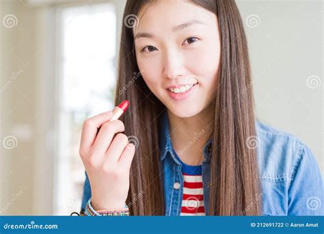 Beautiful Asian Woman Applying Red Lipstick On Lips With A Happy Face