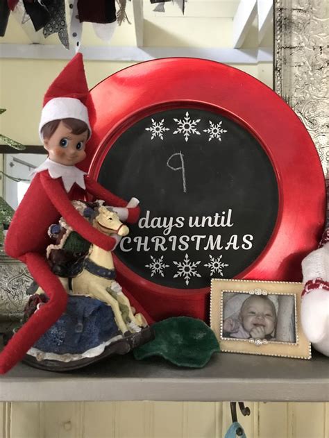 An Elf Sitting On Top Of A Shelf Next To A Christmas Sign And Other