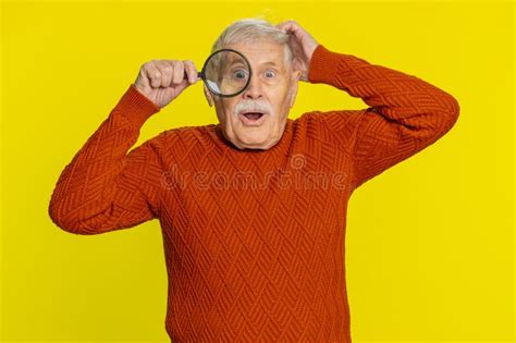 Senior Old Man Holds Magnifying Glass Near Face Looking At Camera With