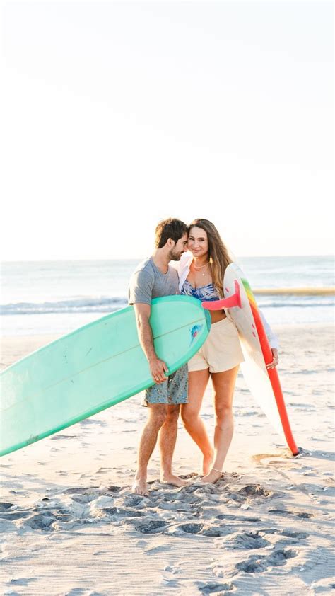 A Man And Woman Kissing While Holding Surfboards On The Beach