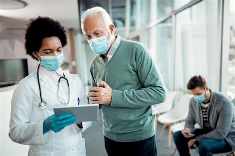 Doctora negra y anciano usando panel táctil mientras usa máscaras