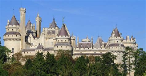 an old castle with towers and turrets is shown from the side, surrounded by trees