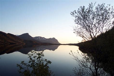 A Lake Surrounded By Mountains And Trees At Sunset