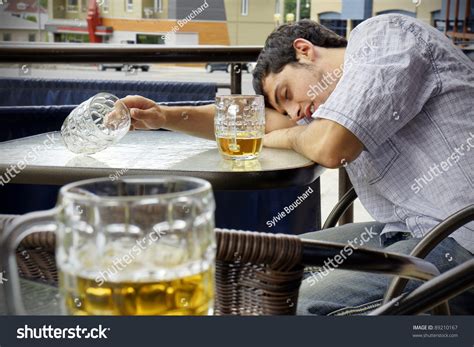 Young Man Passed Out Drunk With Beer Bocks On The Glass Table Of An