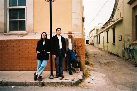 Three People Standing Next To Each Other Near A Lamp Post On The Side