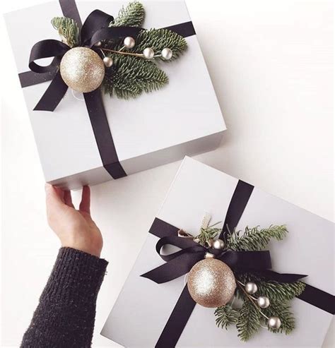 Two White Boxes With Black Bows And Ornaments On Them Are Being Held By