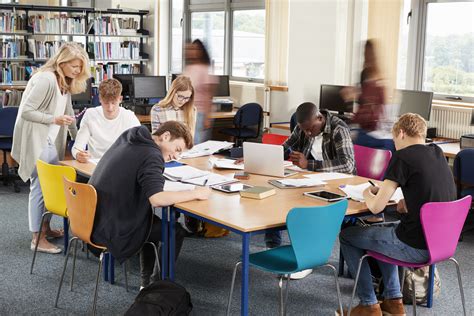 Busy College Library With Teacher Helping Students At Table