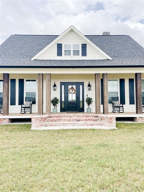 A White House With Black Shutters On The Front Porch And Two Chairs In