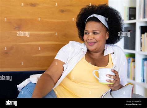 Happy Plus Size African American Woman Relaxing On Sofa Holding Mug