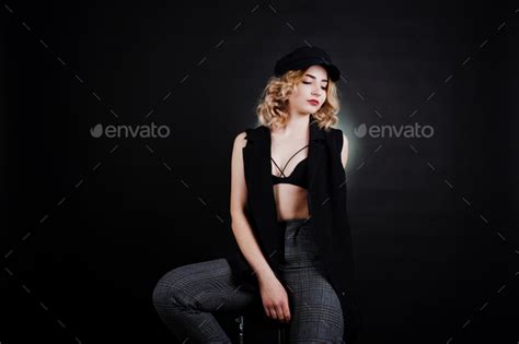 Studio Portrait Of Blonde Girl In Black Wear Bra And Cap Against Dark Background Stock Photo