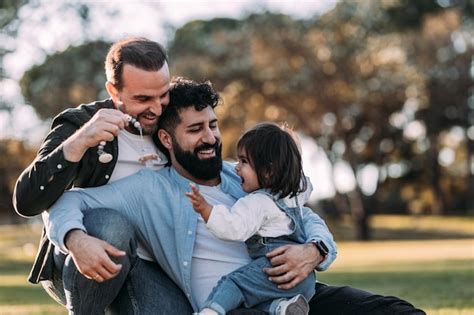 Família gay masculina abraçando e brincando sua filha no parque Foto Premium