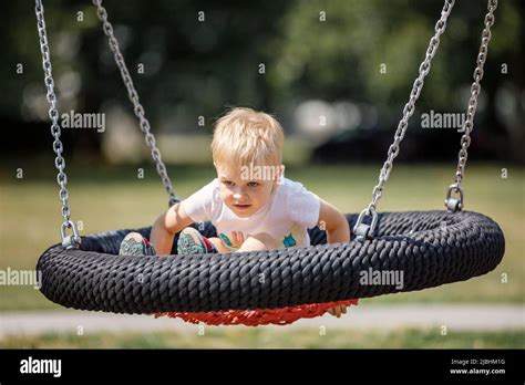 Little Blonde Boy Playing Happily On Large Nest Swing At City