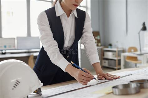Female Engineer Drawing Blueprints And Plans At Workstation In Office