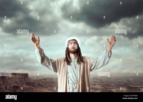 Jesus Christ In White Robe Praying With His Hands Up Against Cloudy Sky