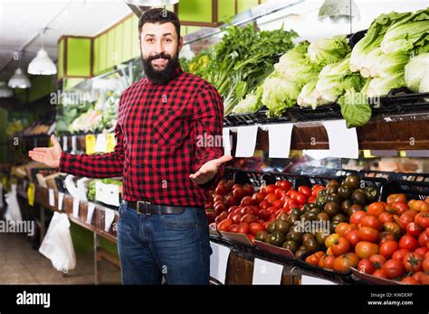 Happy Adult Male Shop Assistant Demonstrating Tomatoes In Grocery Shop