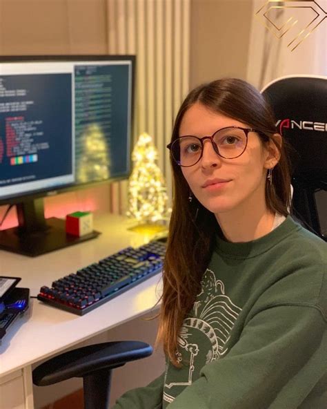 A Woman Wearing Glasses Sitting In Front Of A Computer Desk With Two