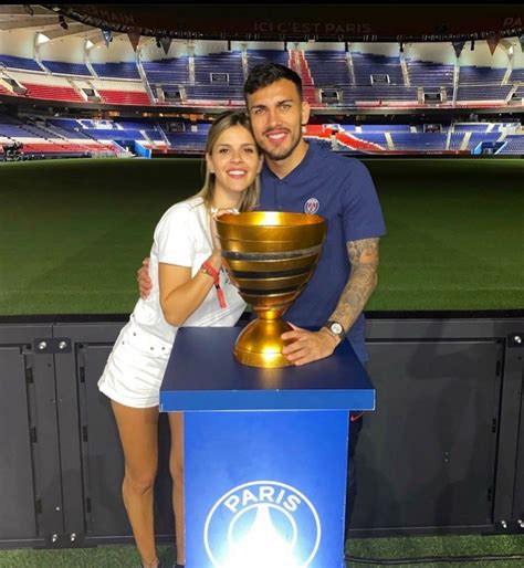 A Man And Woman Standing Next To A Trophy In Front Of A Baseball Field