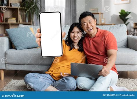 Happy Asian Couple Chilling Together At Home Using Gadgets Stock Photo