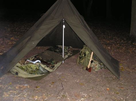 An Army Tent Is Set Up In The Woods At Night With Backpacks And Firewood