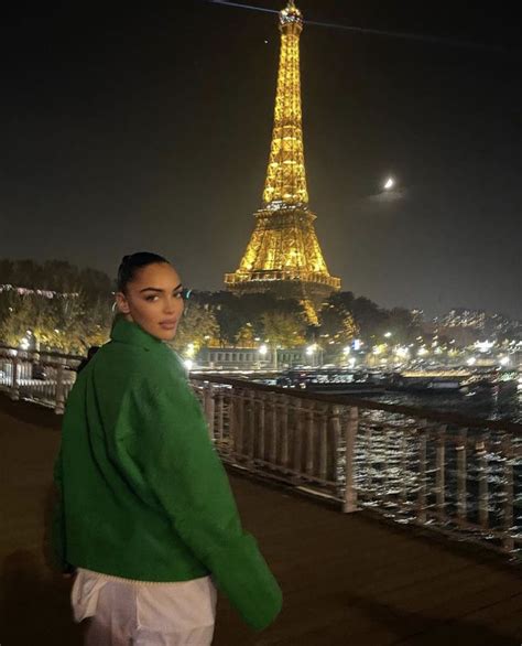 A Woman Standing In Front Of The Eiffel Tower At Night With Her Hands