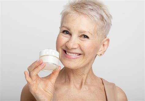Smiling 60s Middle Aged Mature Woman Putting Tightening Facial Cream On