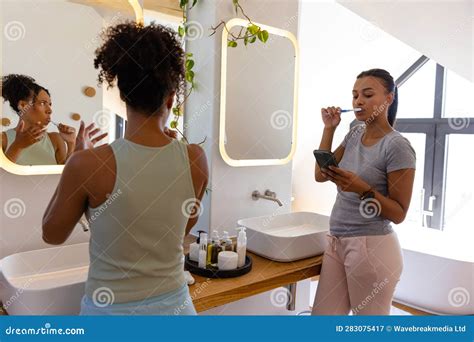 Biracial Lesbian Couple Brushing Teeth And Using Smartphone In Bathroom Stock Image Image Of